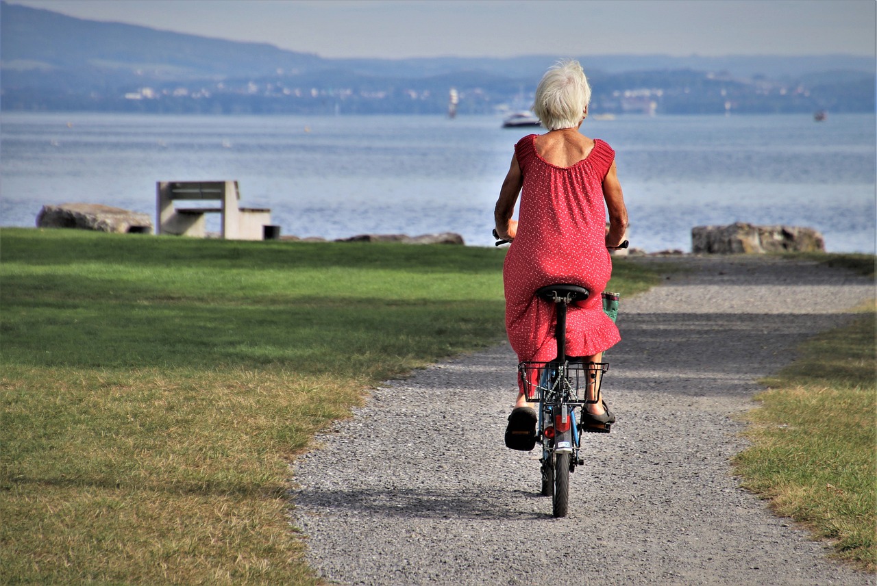older woman riding a bike on a path facing a lake